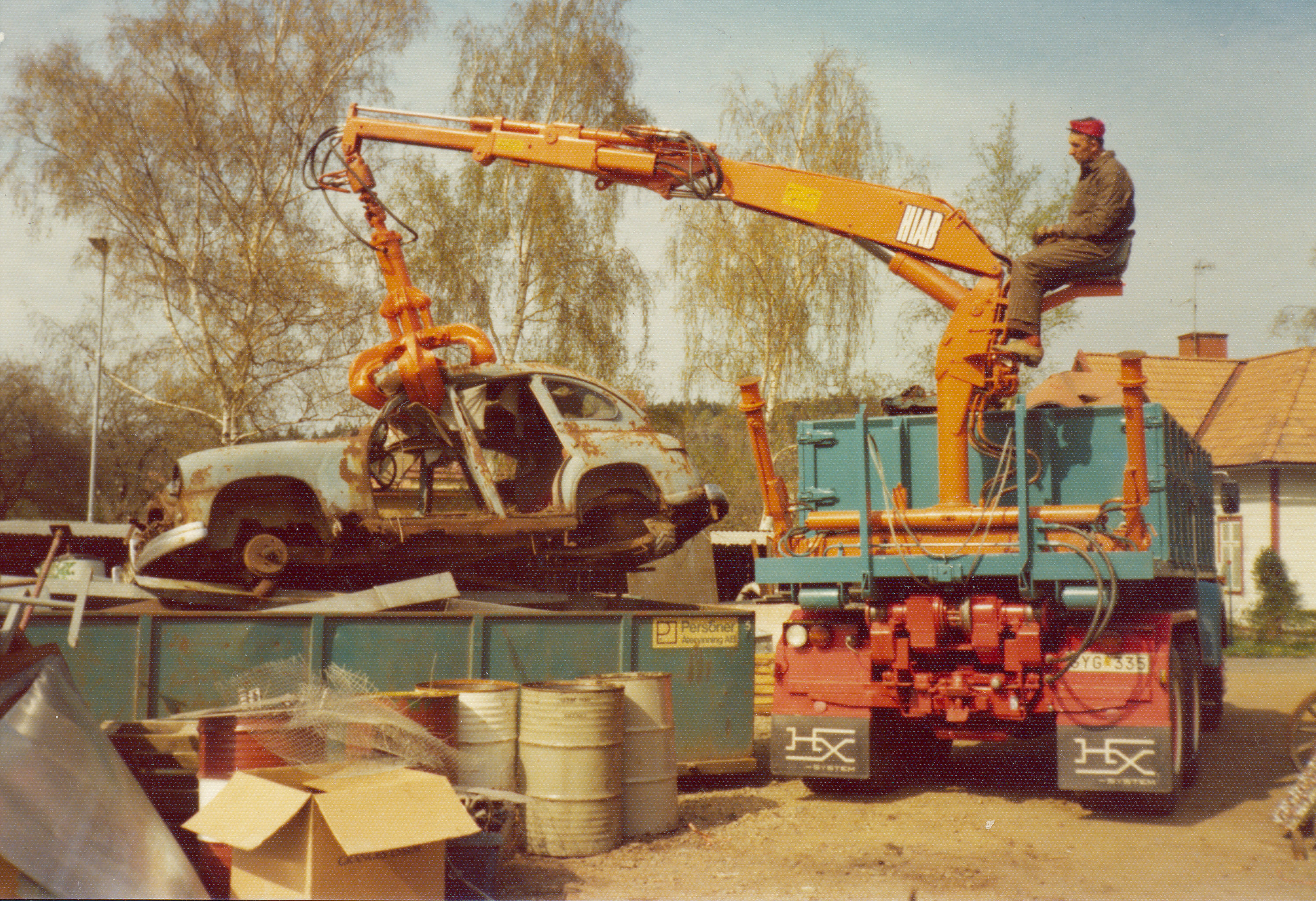A colour archive image showing a scrap car being lifted by a crane and dropped in a container for recycling.