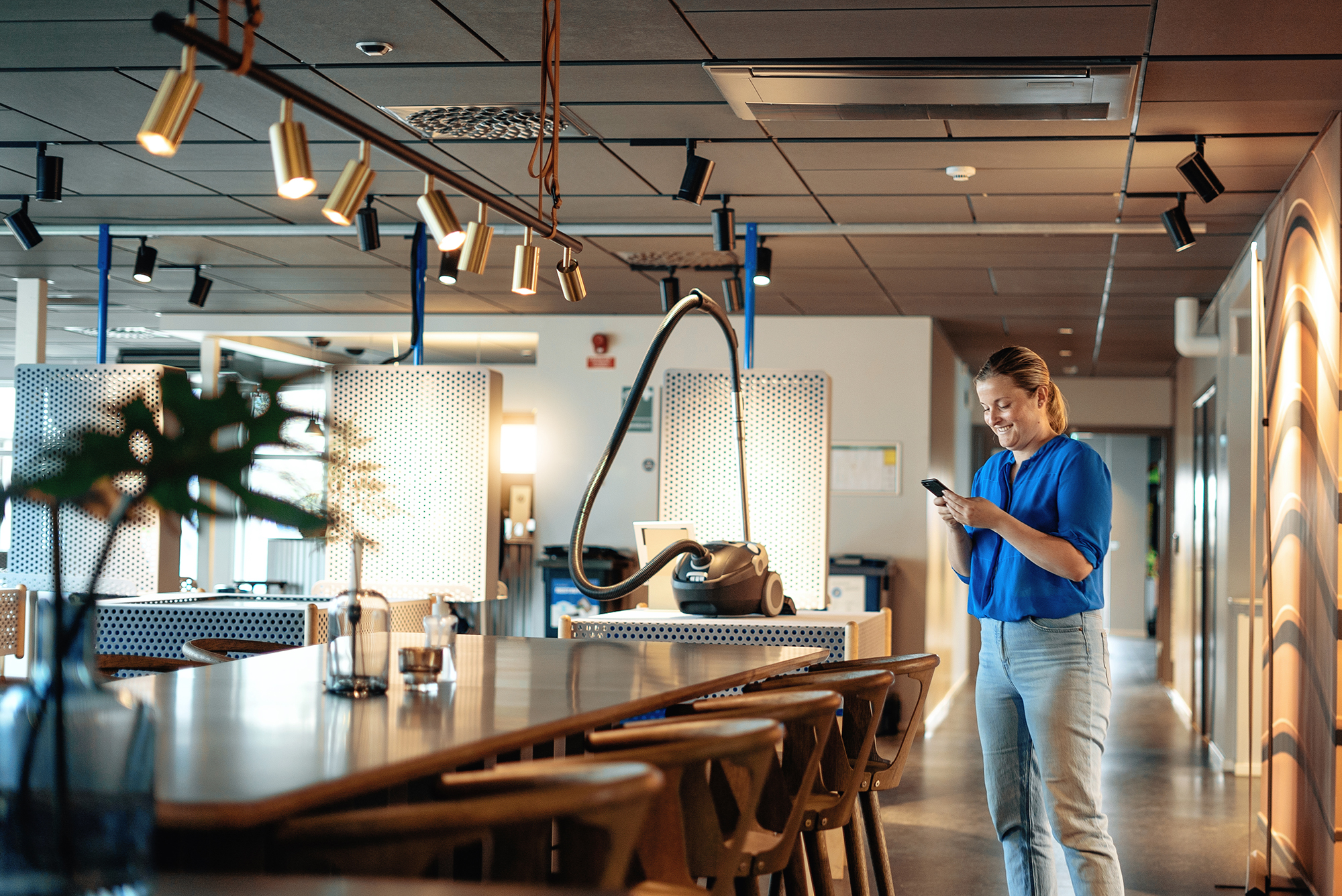 Kvinna som tittar på mobiltelefon i öppet kontorslandskap