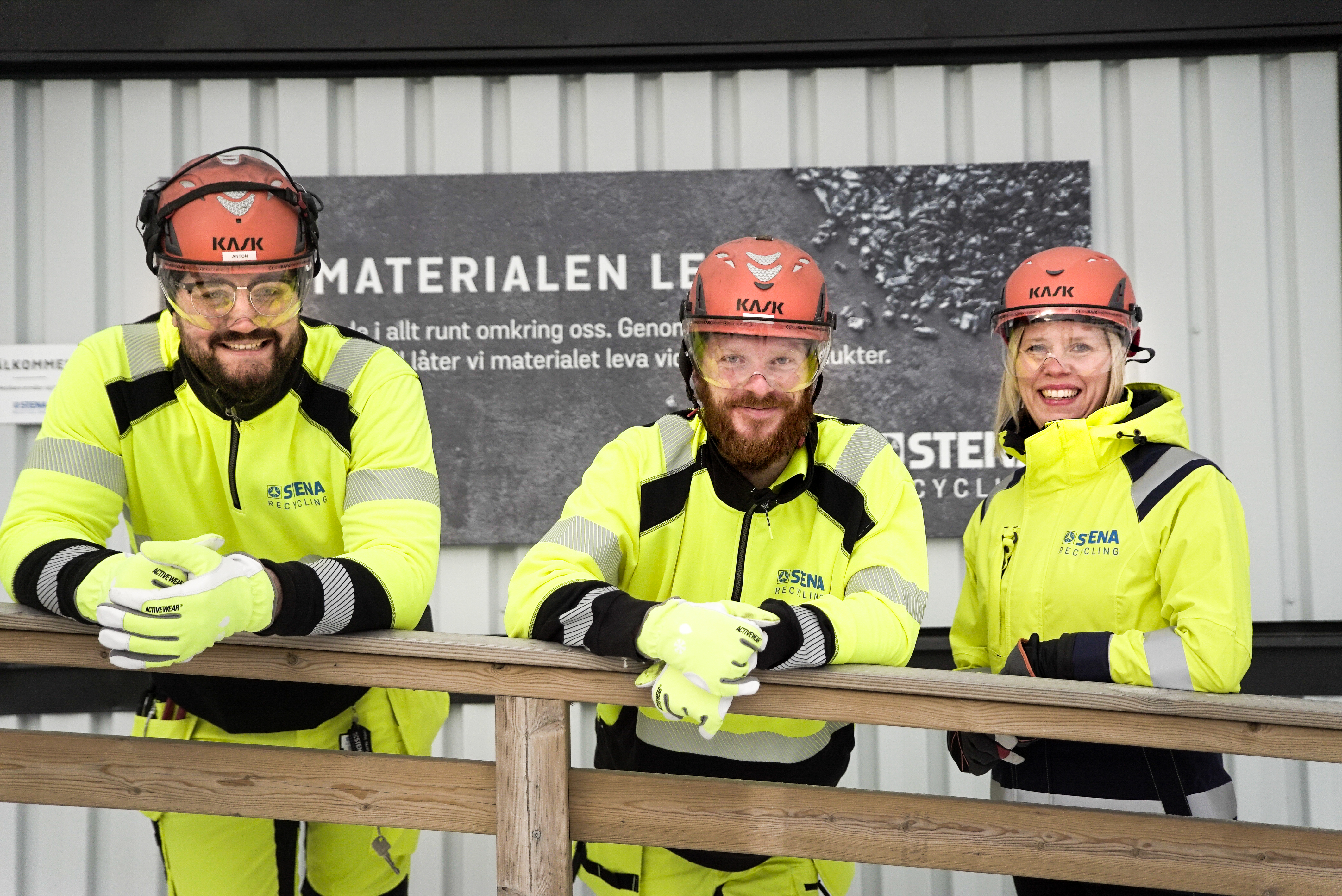 Tvä män och en kvinna i varselkläder som tittar in i kameran