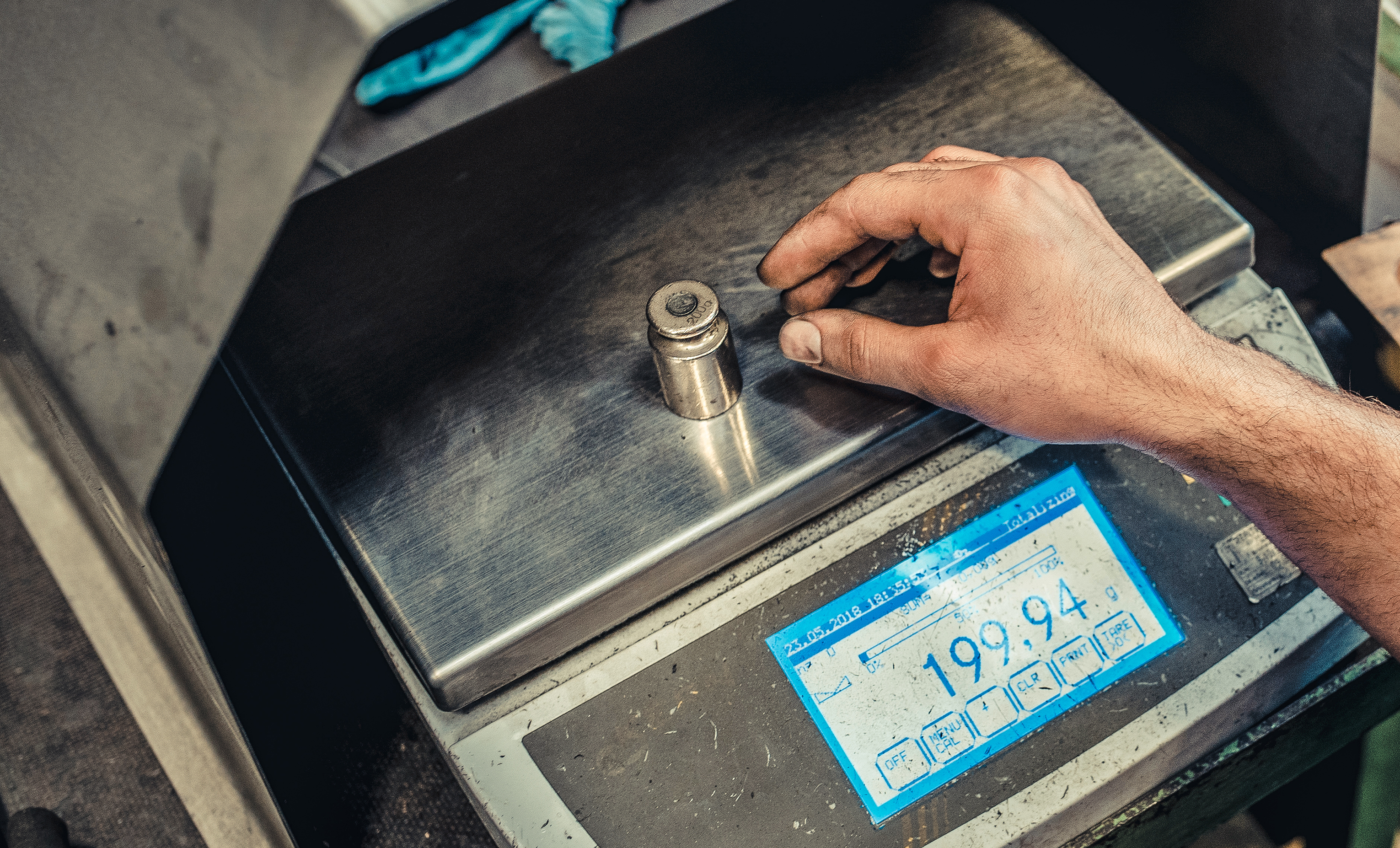 A person places a component on a precision scale, checking the exact weight displayed.