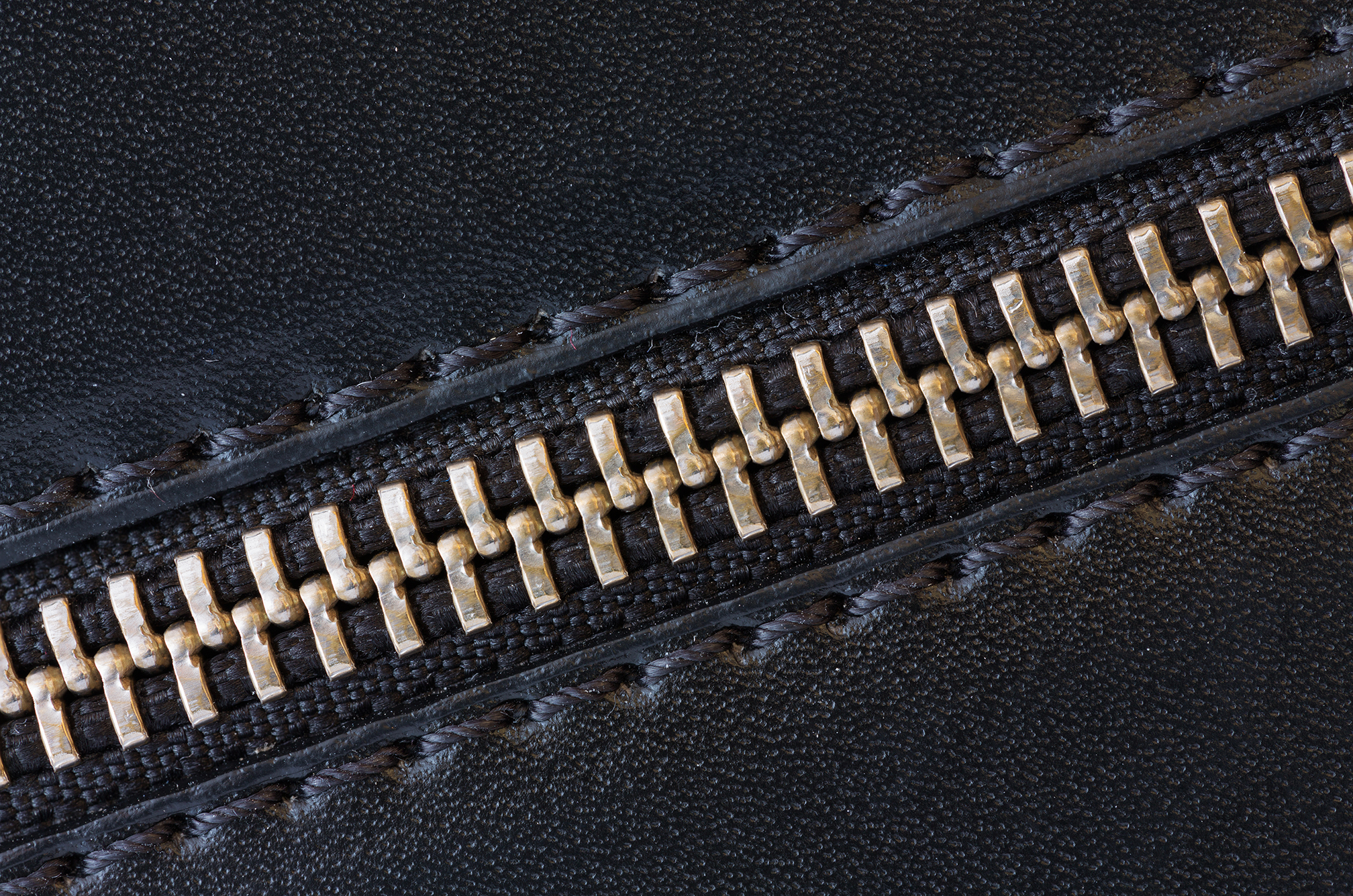 A close-up image of a black faux leather texture featuring a metallic zipper with gold teeth.