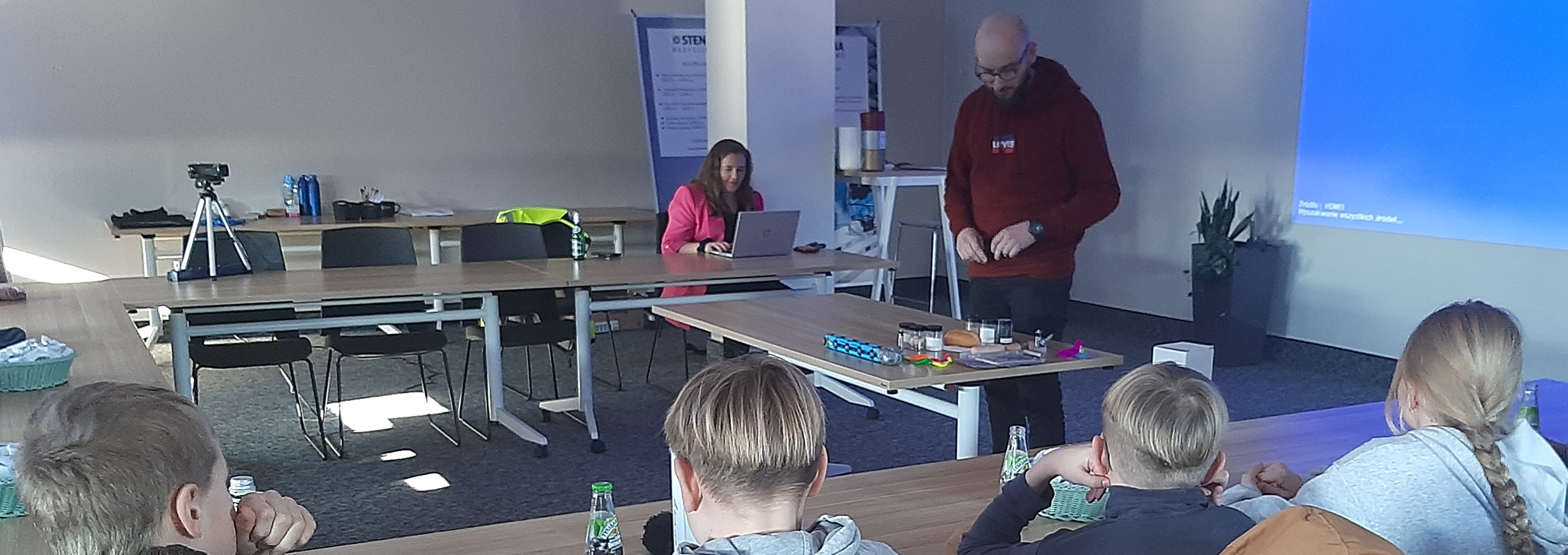 Zdjęcie przedstawia prowadzących wykład oraz dzieci, które oglądają i przysłuchują się prelekcji