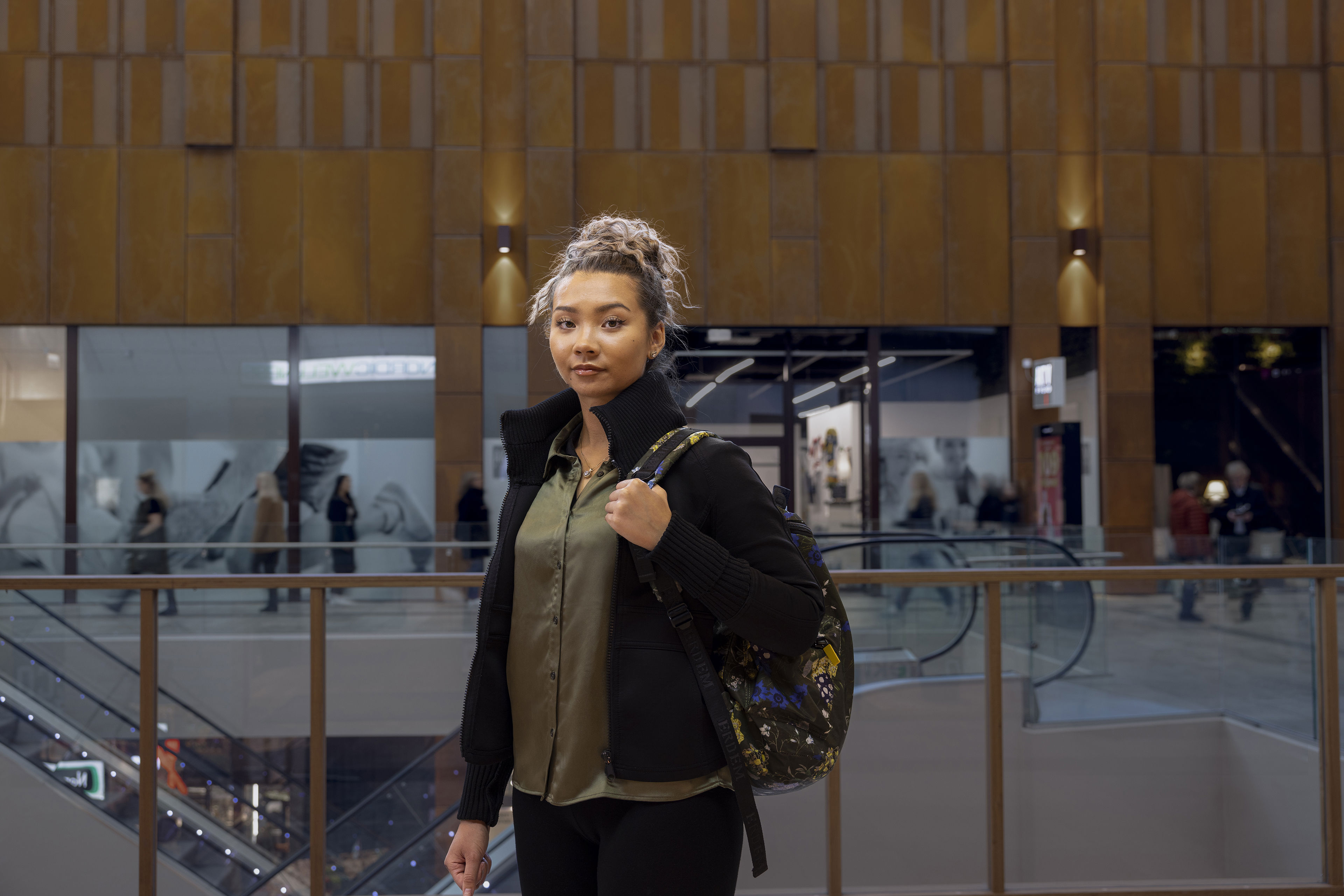 A young woman standing in a shopping centre stares directly into the camera.