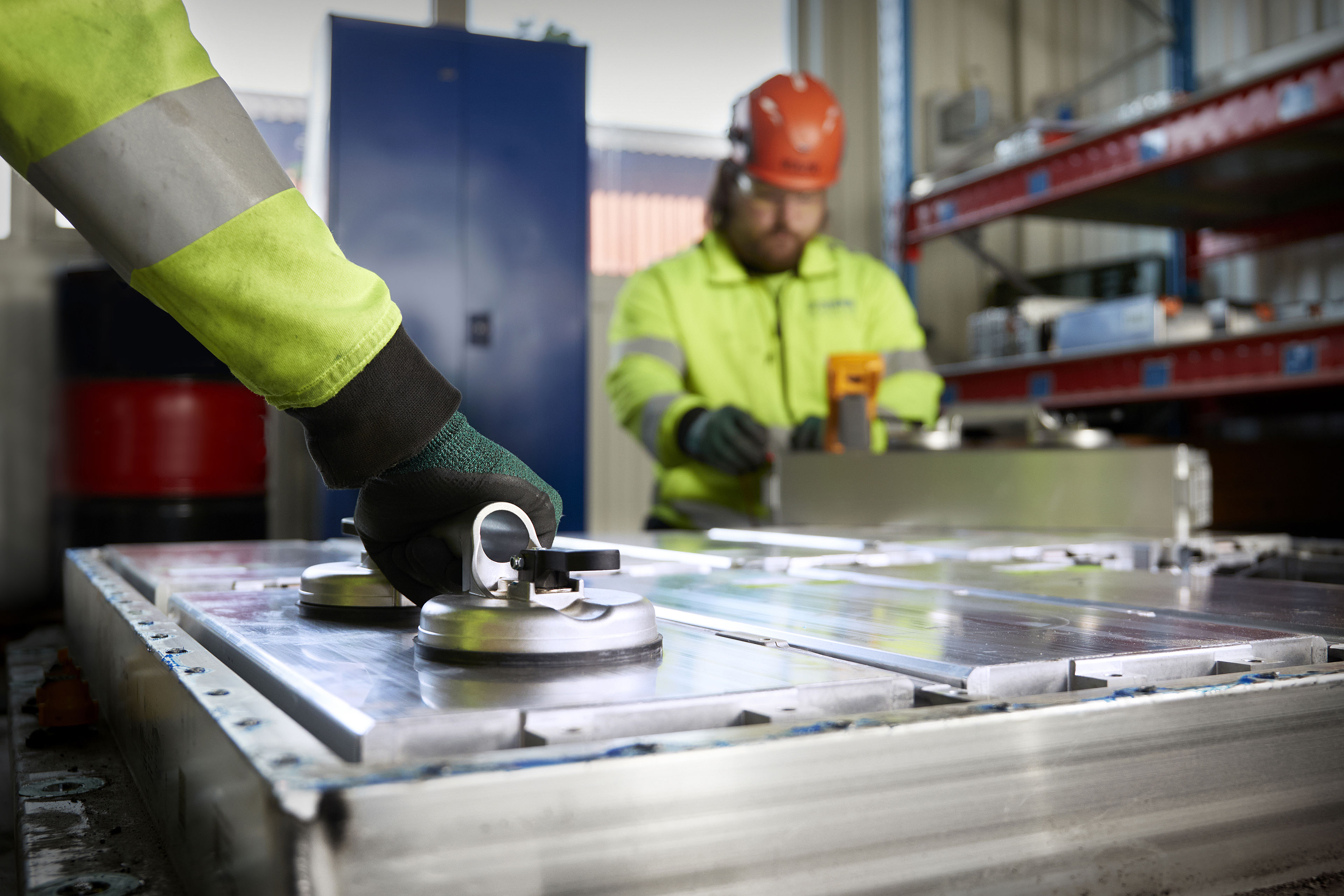 To Stena Recycling experts in protective clothing work on discahrging and dismantling a lithium-ion vehicle battery.