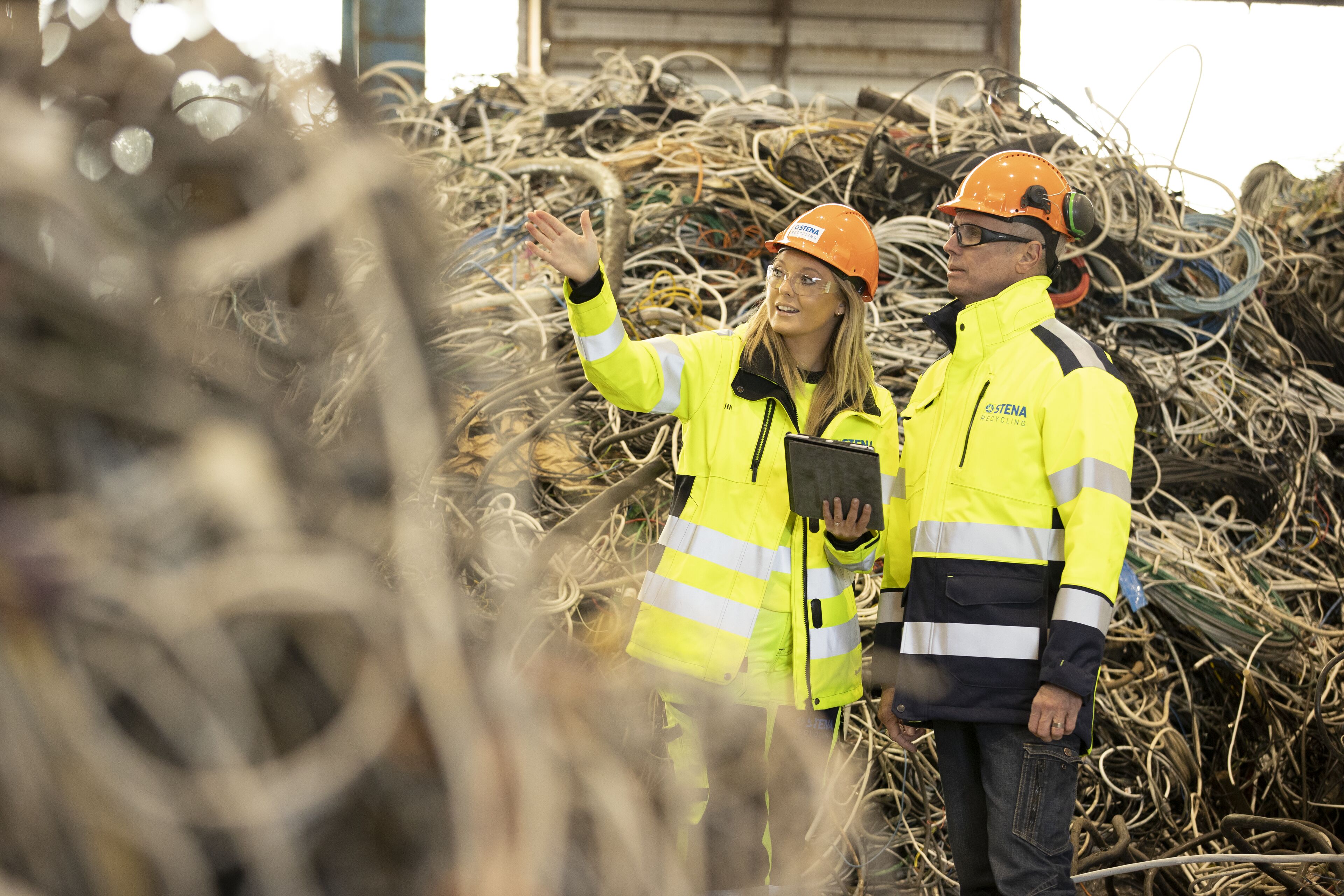 A female Stena Recycling employee driving a waste collection truck talks with a male colleague standing nearby.