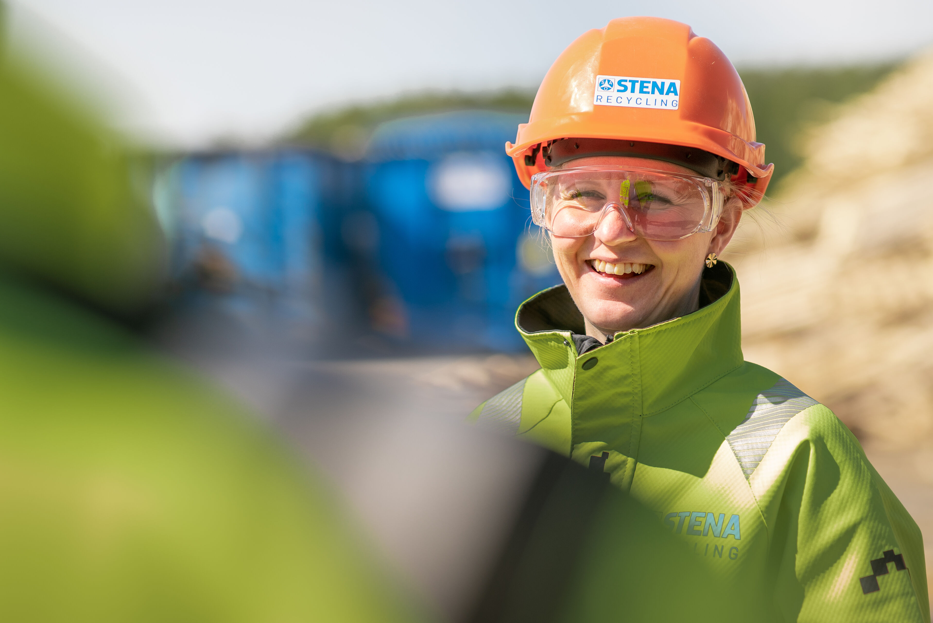 Tre medarbetare i varselkläder framför blå Stena-container